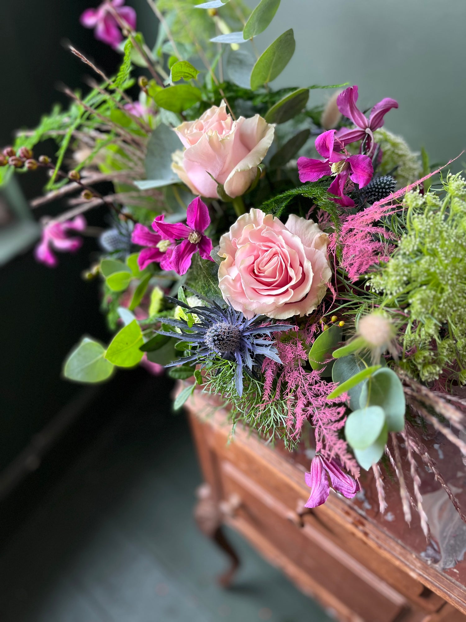 spray of flowers with pink roses and purple flowers on a wooden surface